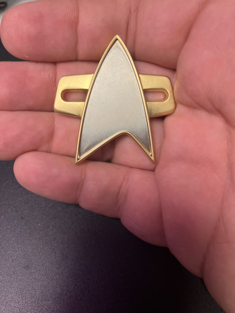 A right hand on a black background with a First Contact-era Starfleet comm badge 
