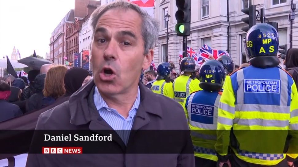 Daniel Sandford reporting on BBC News about the far-right rally in London while the poster for Clarkston with Joe Locke outside The Trafalgar Theatre can be seen in the background.
