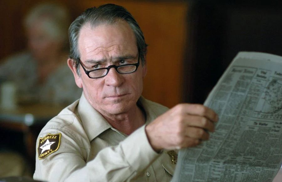 Tommy Lee Jones in No Country for Old Men looking up disdainfully from his newspaper 
