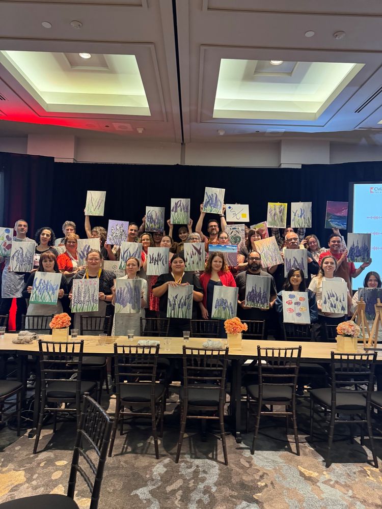 CMG Members stand together holding up paintings on canvas of lilacs.