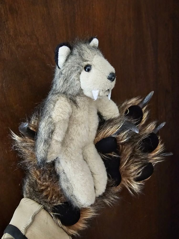 A photo of a cute werewolf plushie being held by a realistic werewolf paw. 