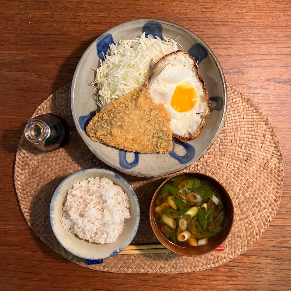 お皿の上に アジフライ・目玉焼き・千切りキャベツ
お皿の横にしょうゆ差し　手前にごはんと味噌汁　GohanClub