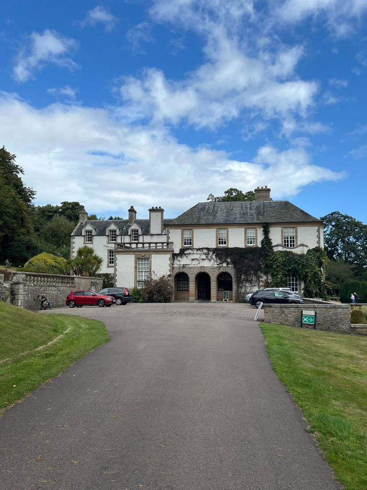 An old Edwardian house in the Scottish country side. A drive way with several cars run up to the front door 