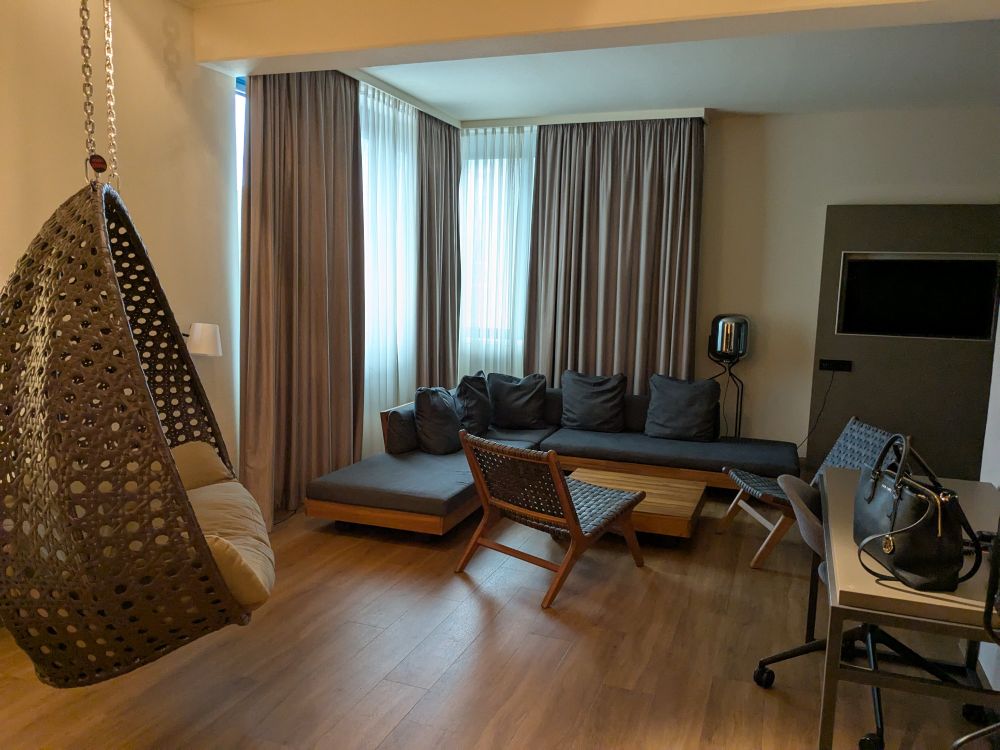 Suite Eingang. Links ist eine Hängeschaukel. Vorne eine Sofalandschaft. Links in der Ecke die großen Fenster. Rechts ein Schreibtisch. 
Rechts im die Ecke ist dann das Bett. Nicht im Bild. 