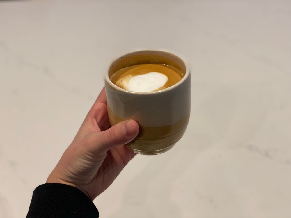 my hand holding a homemade yellow cup, filled with a latte 
