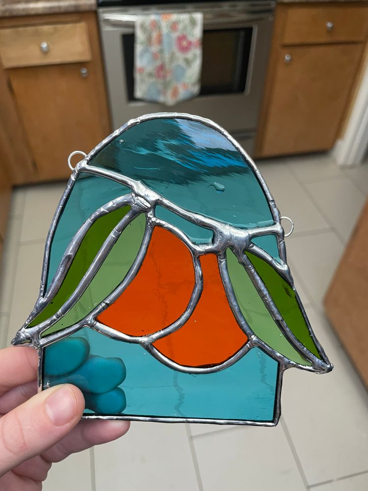 freshly cleaned stained glass piece of 2 oranges & leaves. it hasn’t been finished with patina yet so the solder lines are still silver. 