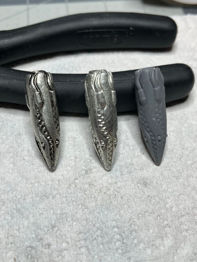Photos of three copies of a missile shaped creature. the original 3d print is on the far right, the two pewter copies are on the left. The far left copy has an antique finish. 