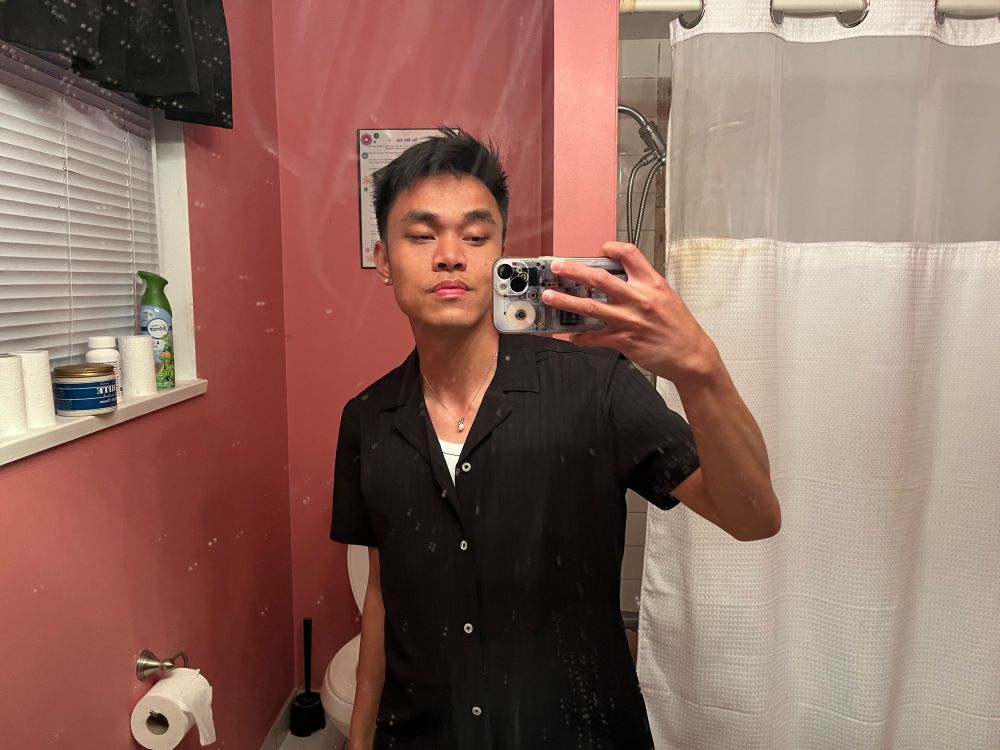 Brandon is at one of his besties birthdays, he is wearing a black short sleeve shirt and white tank top, taking a mirror selfie in said bestie’s bathroom 