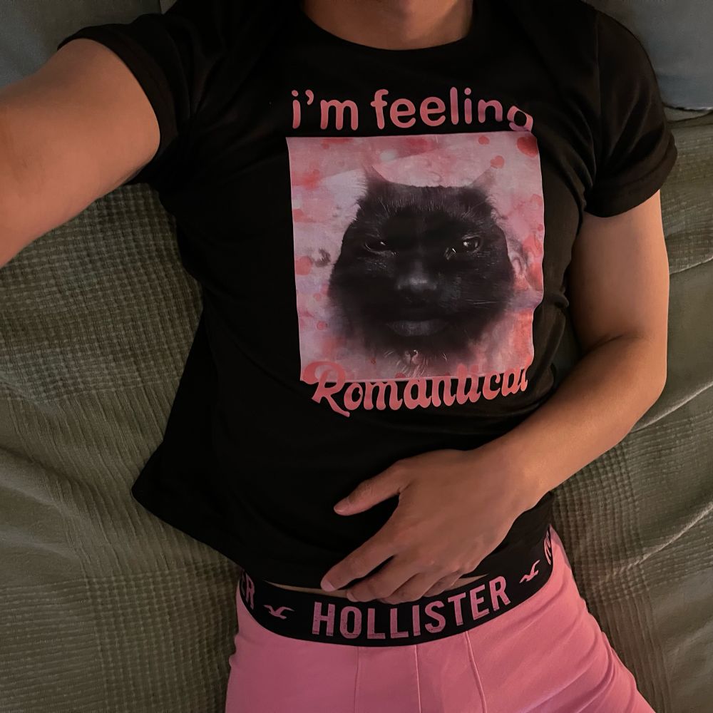 Headless Brandon showcasing his pink Hollister boxer briefs in a black tee featuring a black cat over a pink background that says “i’m feeling romantical”