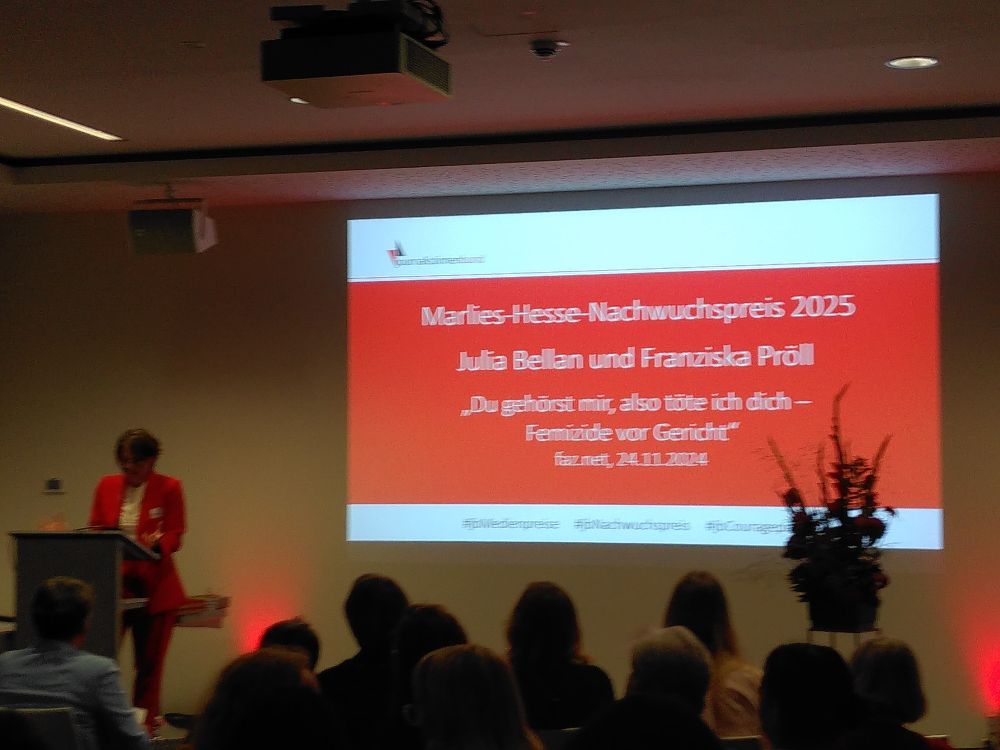 Paula Lochte, Preisträgerin des letzten Jahres, hält die Laudatio für Julia Bellan under Franziska Pröll, die den Marlies-Hesse-Nachwuchspreis des Journalistinnenbundes erhalten. Sie trägt einen roten Hosenanzug.