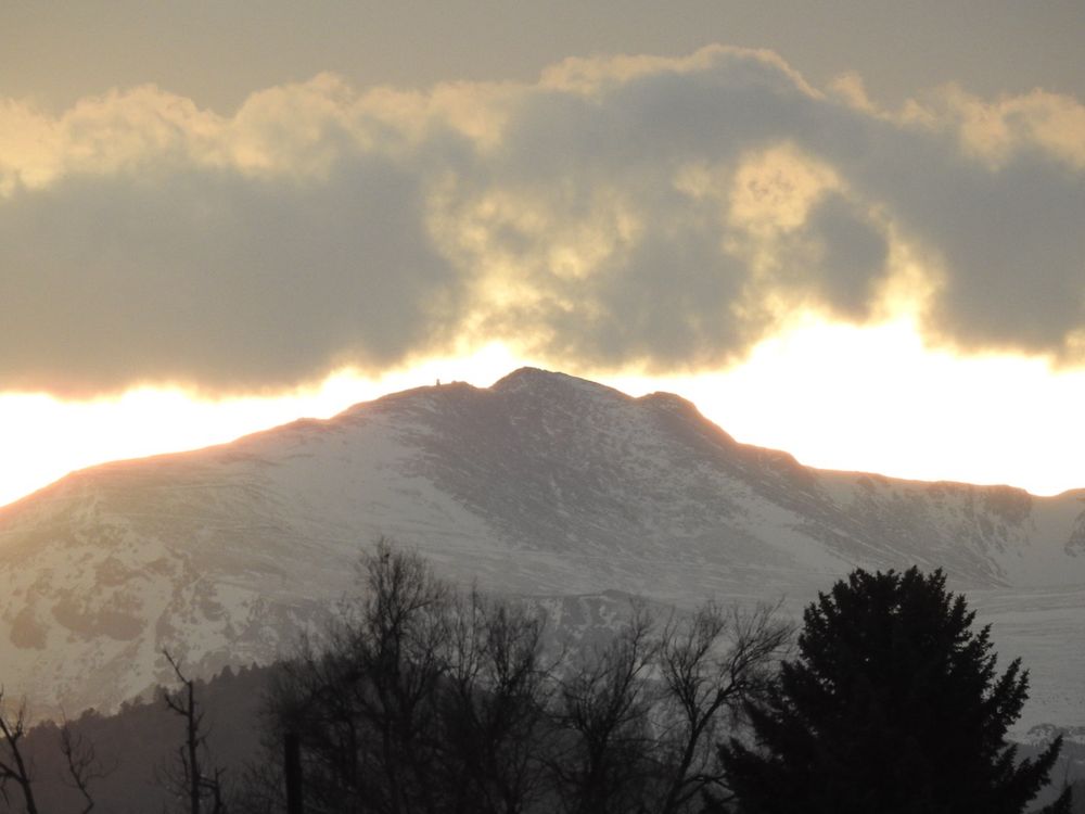 A battle between sunshine and clouds over Mount Blue Sky (formerly Mount Evans) at sunset on Friday, March 21, 2025. Summit features such as the Crest House ruins and the Meyer-Womble Observatory are visible from 36 miles away. Taken with my trusty Nikon Coolpix P900.