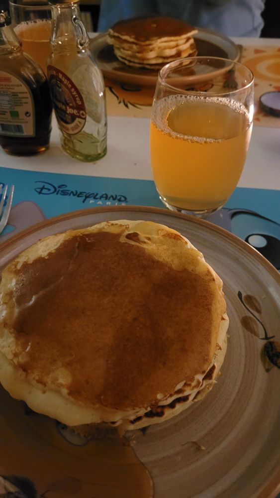 Photo du repas décrit dans le blousque. 2 assiettes, 5 pancakes chacun, un verre de jus de pomme et 2 petites bouteilles de sirop d'érable dont une vide.