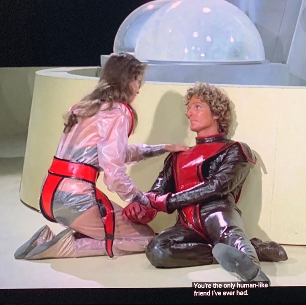 A screengrab from the 1978 film StarCrash. The protagonist, Stella Star, kneels next to her injured companion, Akton. A caption reads: “You’re the only human-like friend I’ve ever had.”