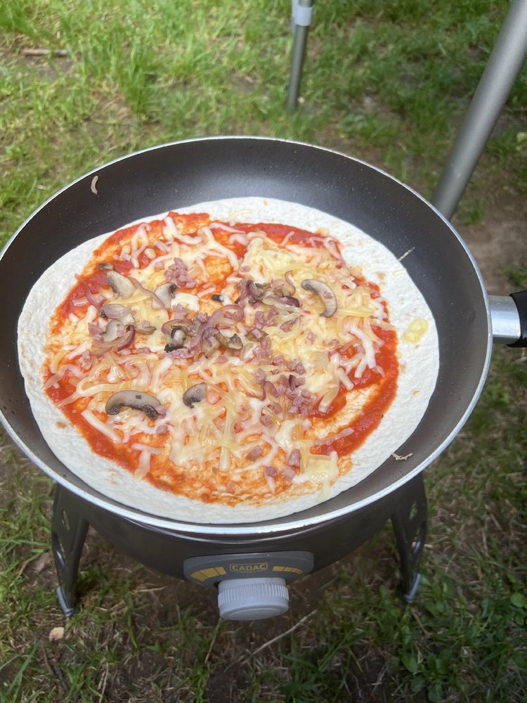 Camping-Gasgrill mit einer Pfanne mit der beschriebenen Mahlzeit drin.