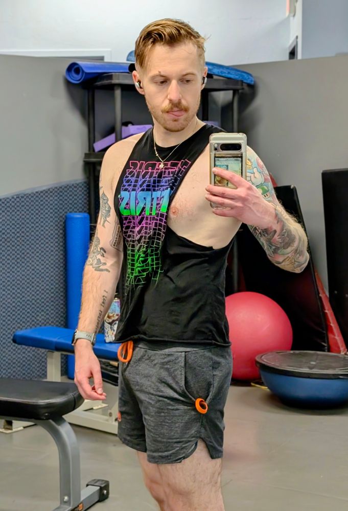 A man sticking their tongue out while taking a picture of themself in a gym mirror. 