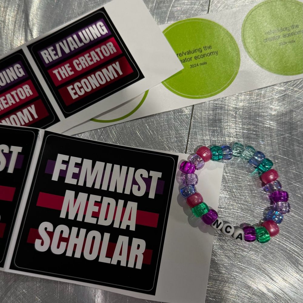 Stickers that read "revaluing the creator economy" and "feminist media scholar" and a beaded friendship bracelet that says 
"NCA"