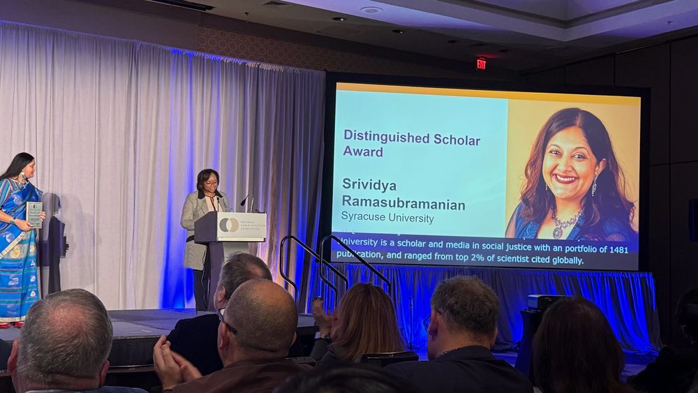Big screen announcing Srivi Ramasubramanian as NCA distinguished scholar. She is standing on stage as Dr. Jeannetta Sims announces at the podium. 