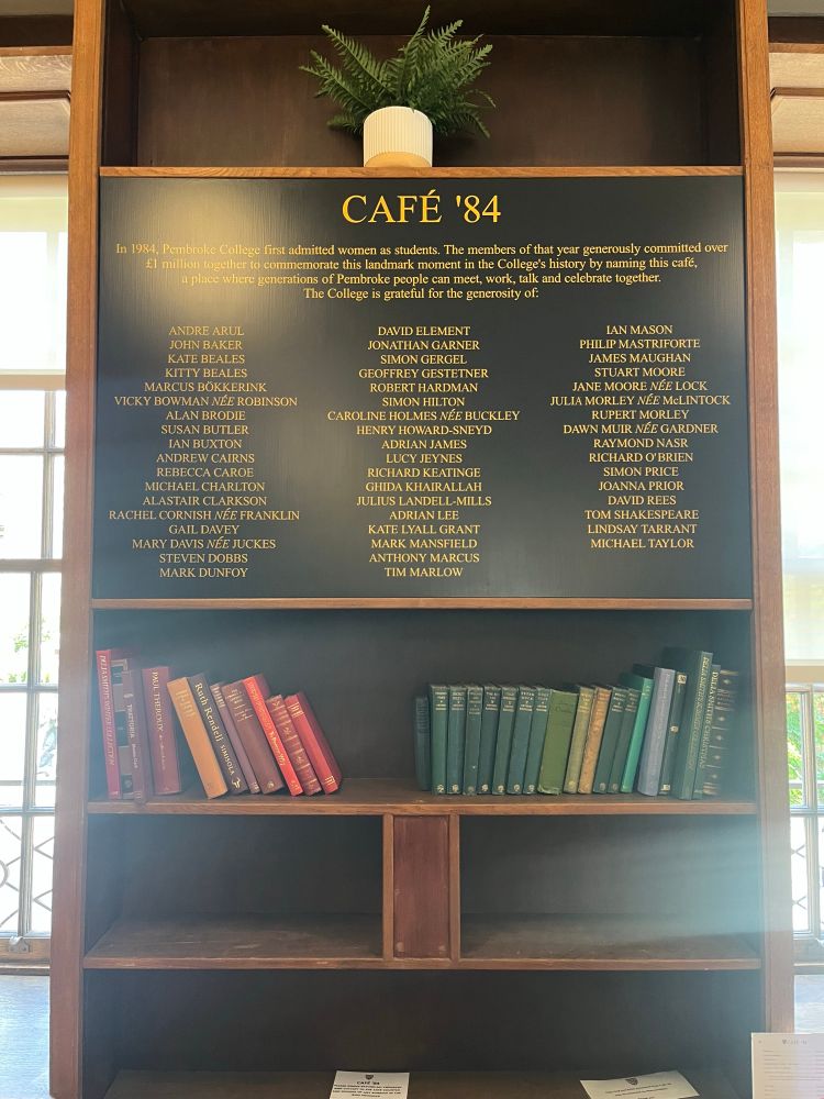 A photo taken inside the Café ‘84, Cambridge. It features a little explanation about the name of the cafe, a list of donors, and a shelf filled with books.