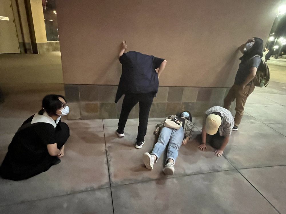 A photo of several Asian adults after seeing the movie "Everything Everywhere All at Once". One of them is in the fetal position, one is laying on the ground in grief. One is leaning up against the wall with exhaustion and another has a hand on their forehead. Another is on all fours. The implication is that the movie hit all of them like a truck.