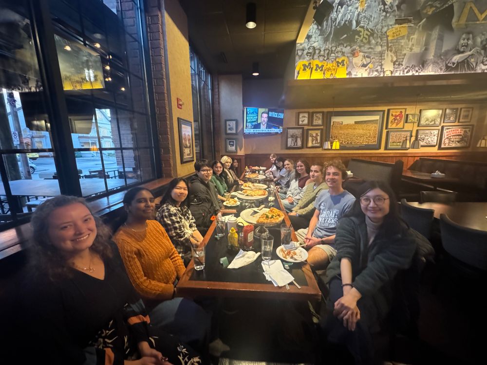 Lauren’s project research team at Pizza House to start off the Fall semester right. 15 individuals are seated at a long table smiling with much pizza and garlic bread. 