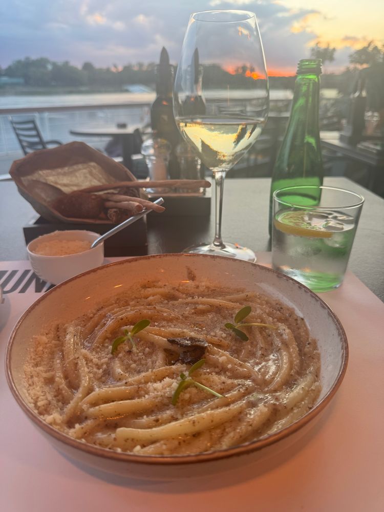 A meal of Istrian (Croatian) pasta with Parmesan and truffle and a glass of Pinot Grigio, and a bright shock of orange sunset over the Danube in the background. 