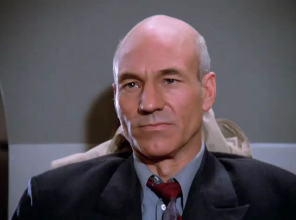 a bald man wearing a suit and tie looks to the side