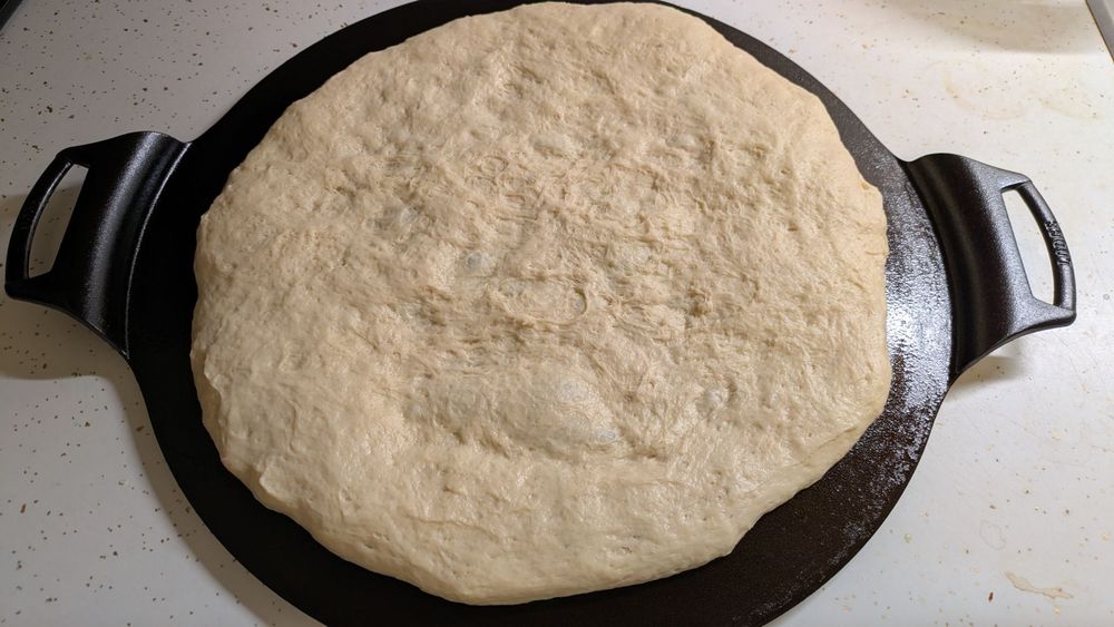 A lump of pizza dough has been spread out over a 15-inch (38-cm) castiron pizza pan. The dough was allowed to ferment for about 18 hours before it was used for the crust.