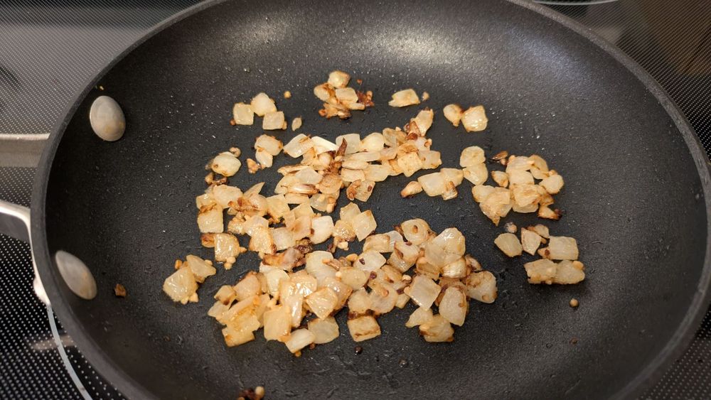 Diced onions and garlic simmer in a pan, browned but not yet caramelized.