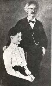 A vintage photo showing a woman (Helen Keller) in a high-collared white shirt seated next to a tall man with a bushy mustache and twinkling eyes (Mark Twain).