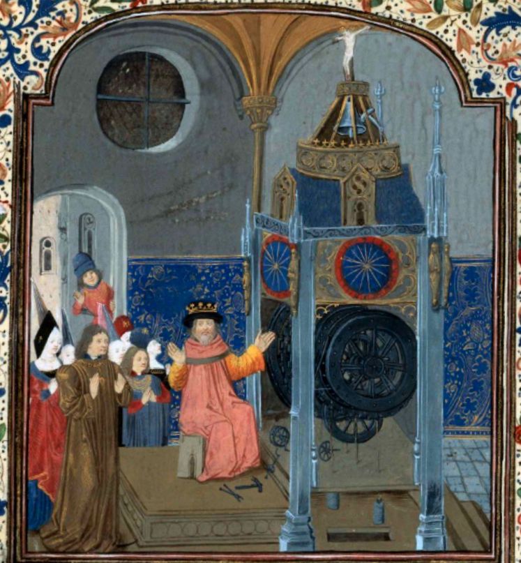 A man sits in front of a very large clock with tools at his feet. He has both arms raised. A crowd of people in late 15th C clothing stand near him, most with their hands folded as though in prayer.