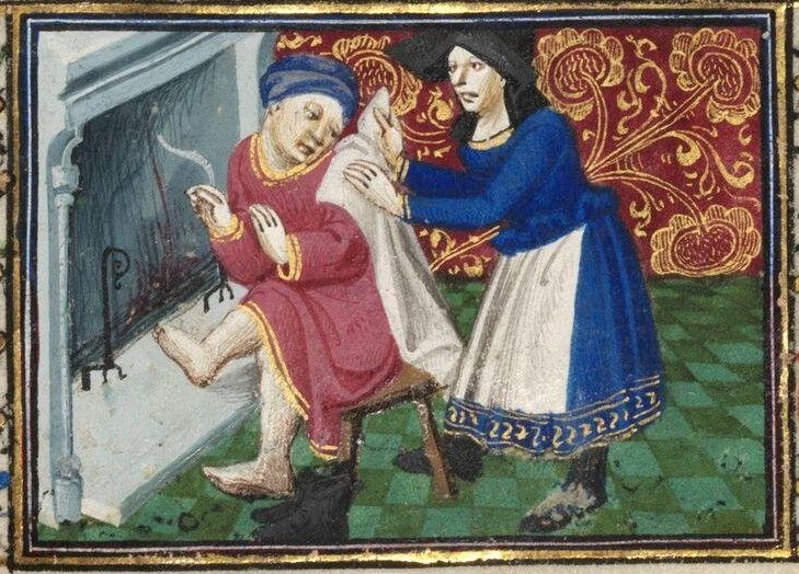Painting in a medieval manuscript. A man sits on a stool with his hands raised towards a small fire in the fireplace. His boots are off and one foot also raised towards the fire. He is looking back as a woman places a towel on his back. There are bits of snow on the floor in front of him and behind her.