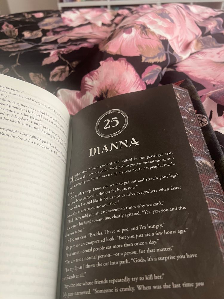 Shot of a book lying open on a black with pink flowers bedspread. 