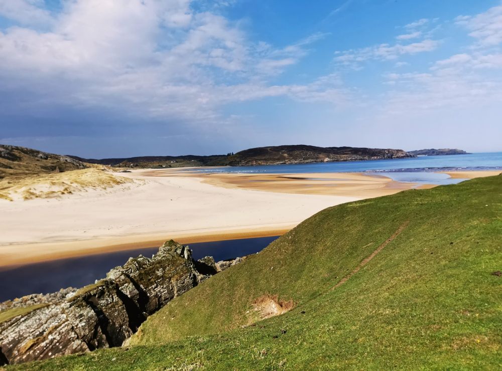 Plage de sable blanc, au 1er plan la pente d'une colline herbeuse