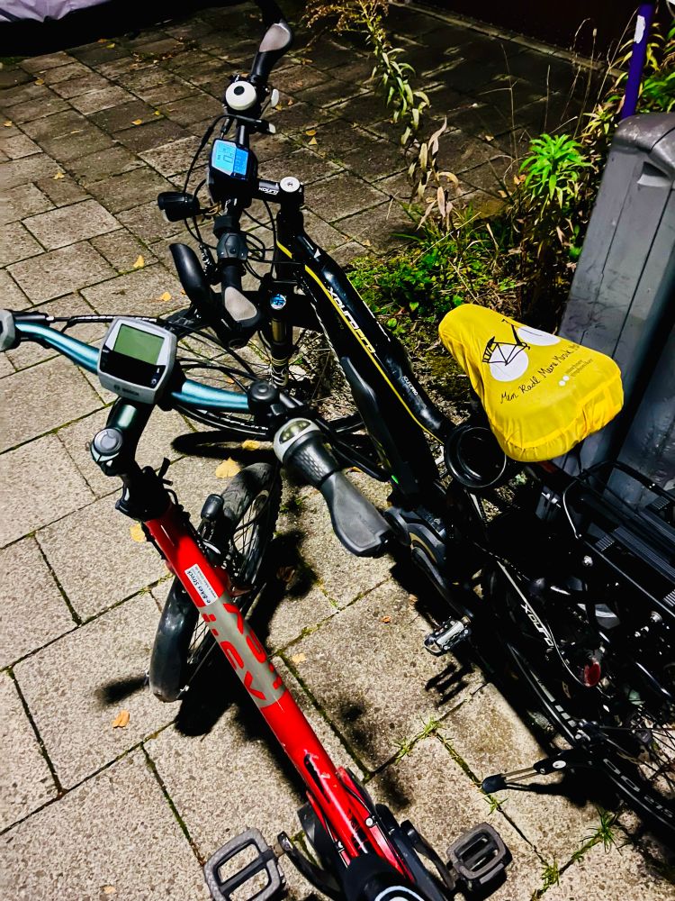 2 E-Bikes, ein kleineres rotes und ein größeres schwarz-gelbes parken nebeneinander.