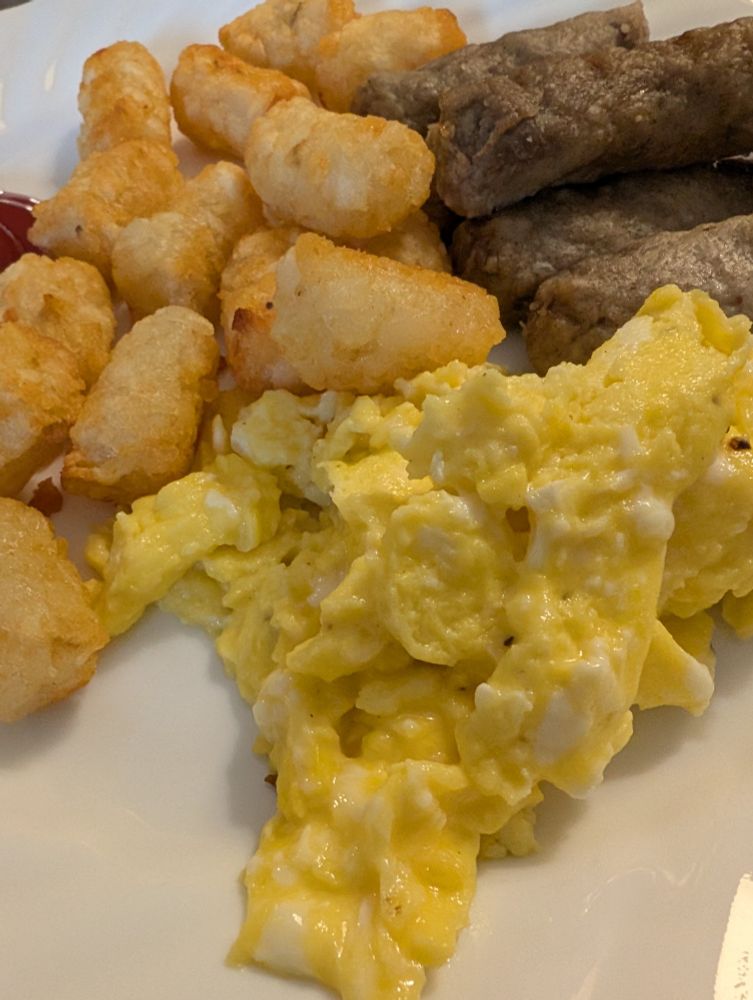 Scrambled eggs, tater tots and turkey sausage on a white plate 