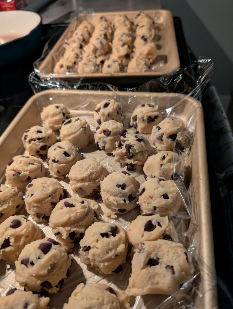 Frozen balls of chocolate chip cookie dough on metal trays lined with saran wrap