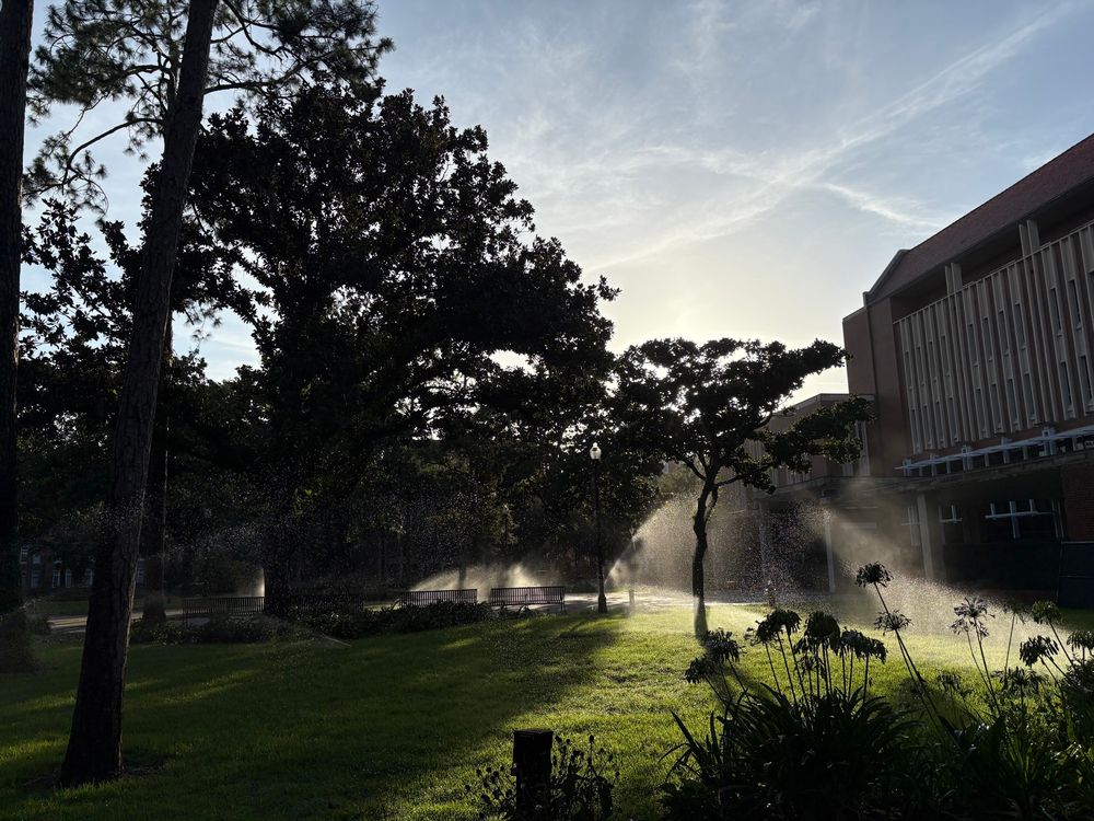 The sun sets in Plaza of the Americas at the University of Florida. The sun rays are shining through the sprinklers. 