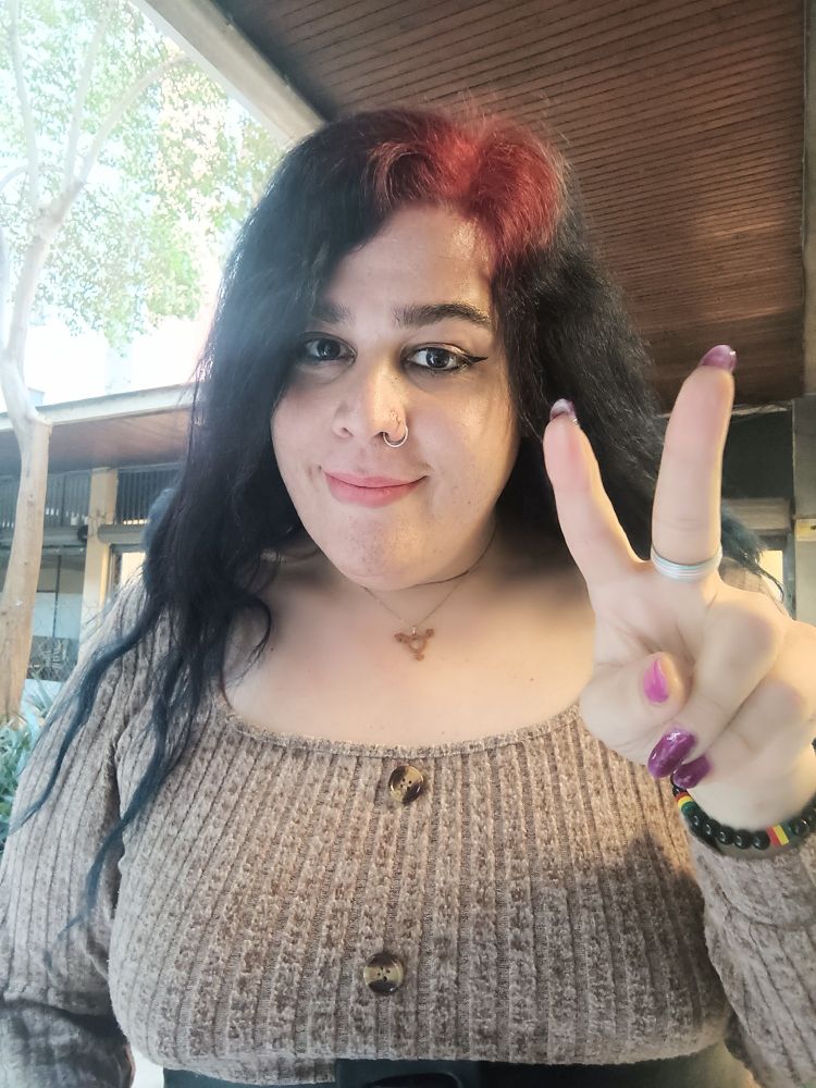 Foto de Clara sonriendo literalmente con los dedos indice y corazón de la mano izquierda haciendo simbolo de victòria. 