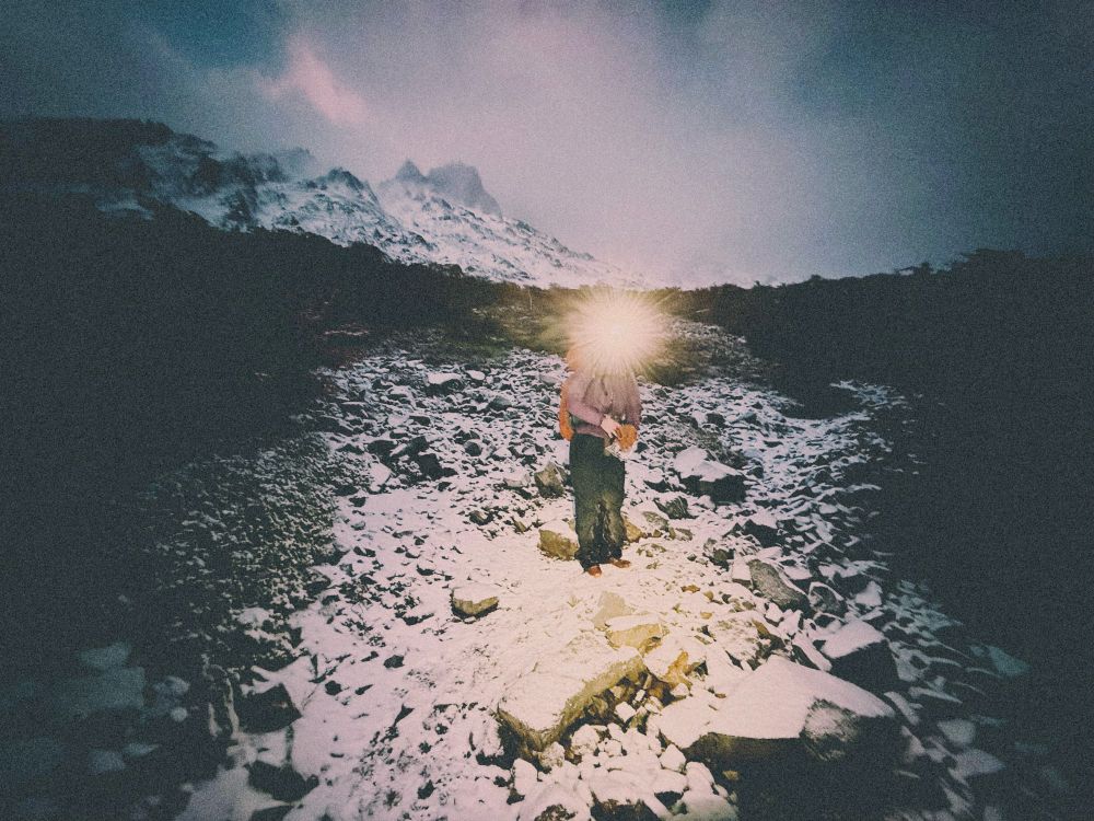 a trekker on a snowy mountain with a headlamp casting glare in the early (dark) morning