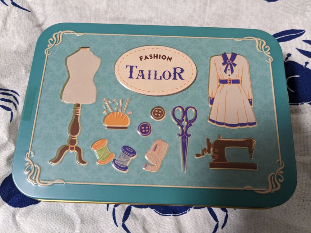 『レトロな路地裏』のファッションテーラー缶。ベース色と絵に描かれてるワンピースやら巻糸やら概念色過ぎてすごい。その他の缶もかわいいぞ。