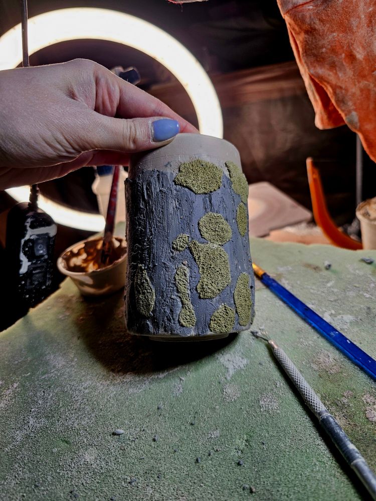 A porcelain pot covered with gray clay texture and moss looking clay texture. 