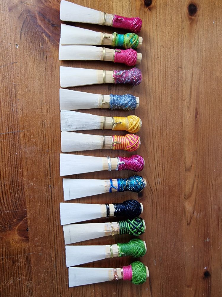 13 bassoon reeds with different coloured thread in a row.