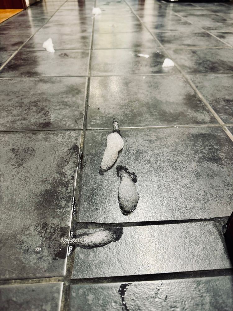 Foto eines gefliesten Bodens auf dem vers. Schaumspuren zu sehen sind