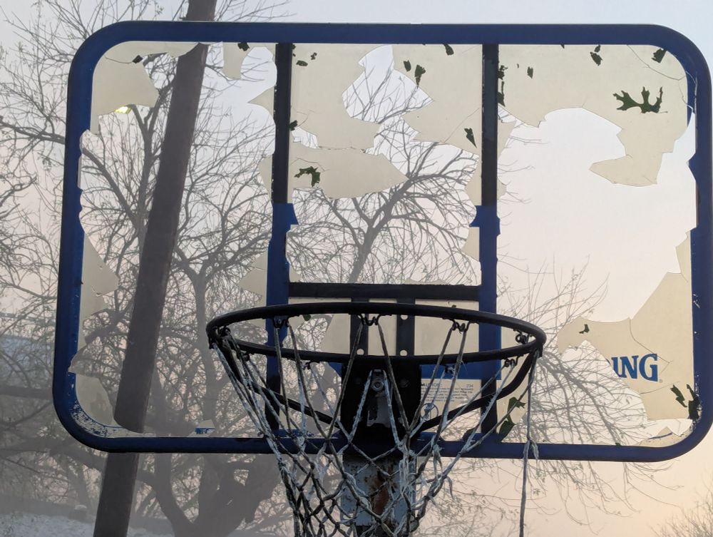 Basketball hoop with a hail damaged backboard.
