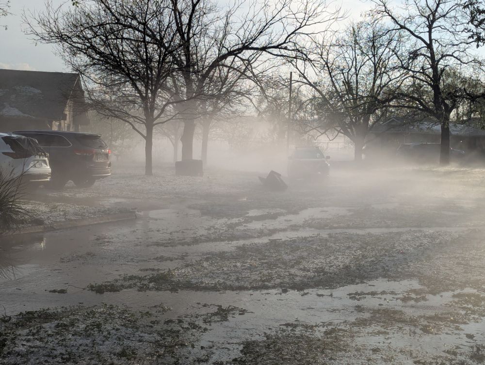A neighborhood street with steam coming off the ground and hail covering everything.