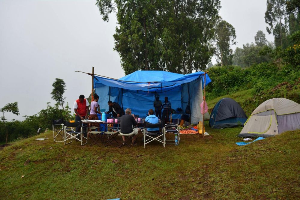 The blue kitchen tent from Sodicho, Ethiopia. To the right team tents. Multiple people enjoying breakfast in the foggy morning.