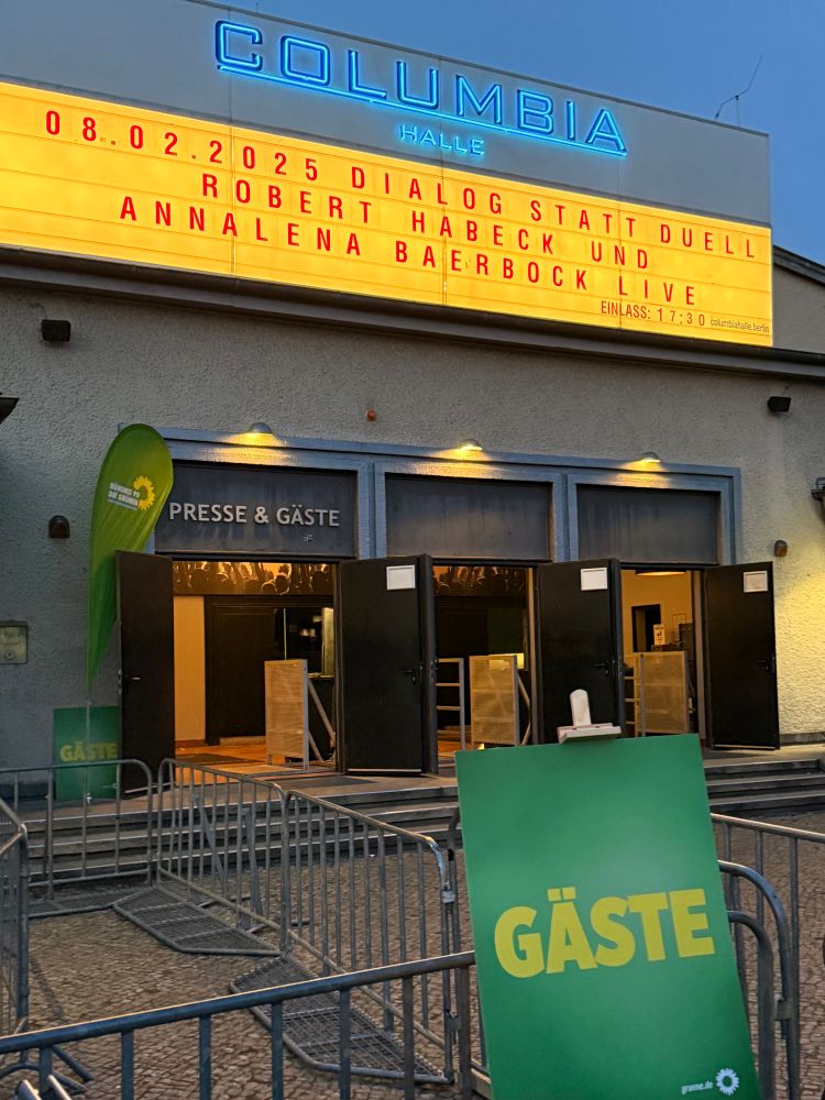 Foto vom Eingang der Columbiahalle in Berlin. Auf dem beleuchteten Schild über der Tür steht: 
„08.02.2025
DIALOG STATT DUELL
ROBERT HABECK UND
ANNALENA BAERBOCK LIVE“