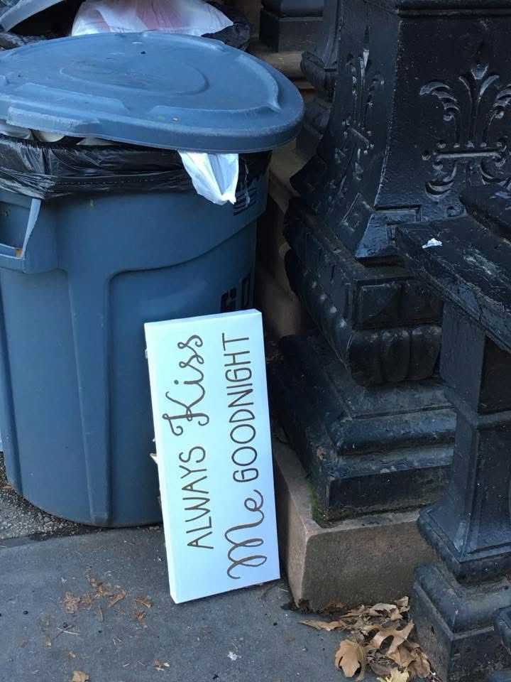 Store bought novelty sign leaning on its side by trash and in NYC reads: Always Kiss Me Goodnight 