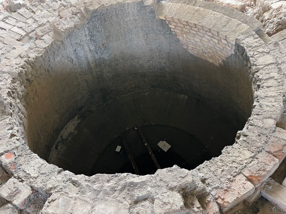 Photo looking down into a large old circular hole, which is the remains of Abraham Darby’s furnace. It is brick built. Old bricks and cement line the edges of the photograph.
