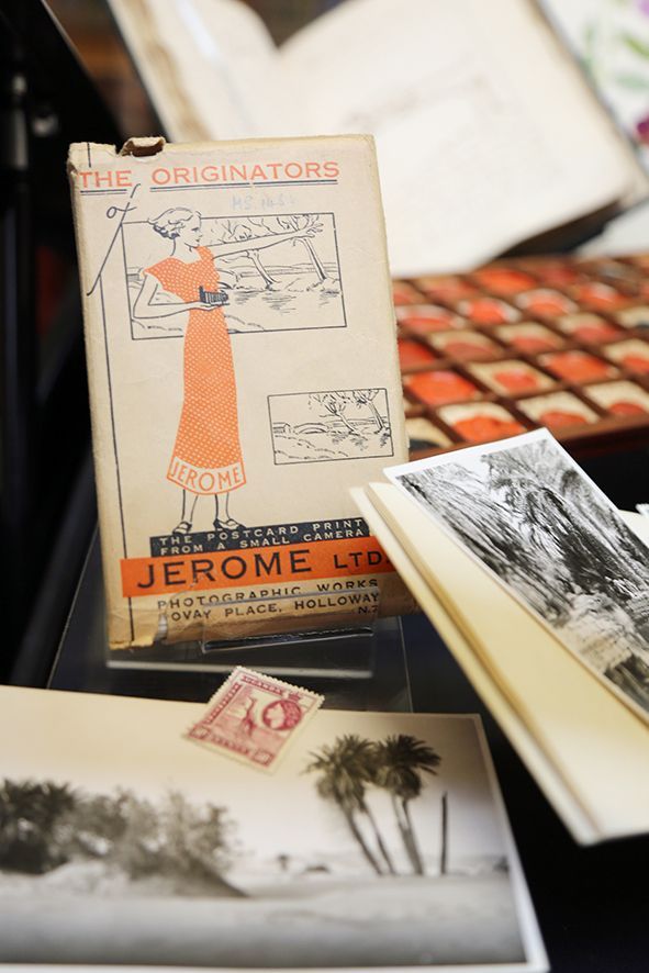 A postcard print package with an image of a wome in an orange dress holding a camera. It is among photos and stamps, as well as seals from Linnaeus' correspondence.